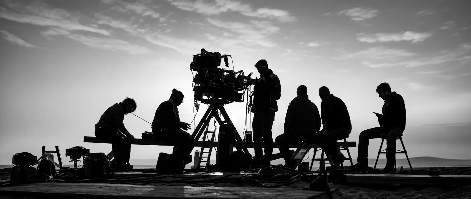 Silhouettes of a film crew around a camera on a tripod